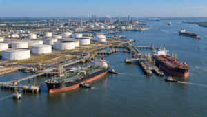 Crude oil tankers at a coastal terminal beside storage tanks and a refinery.